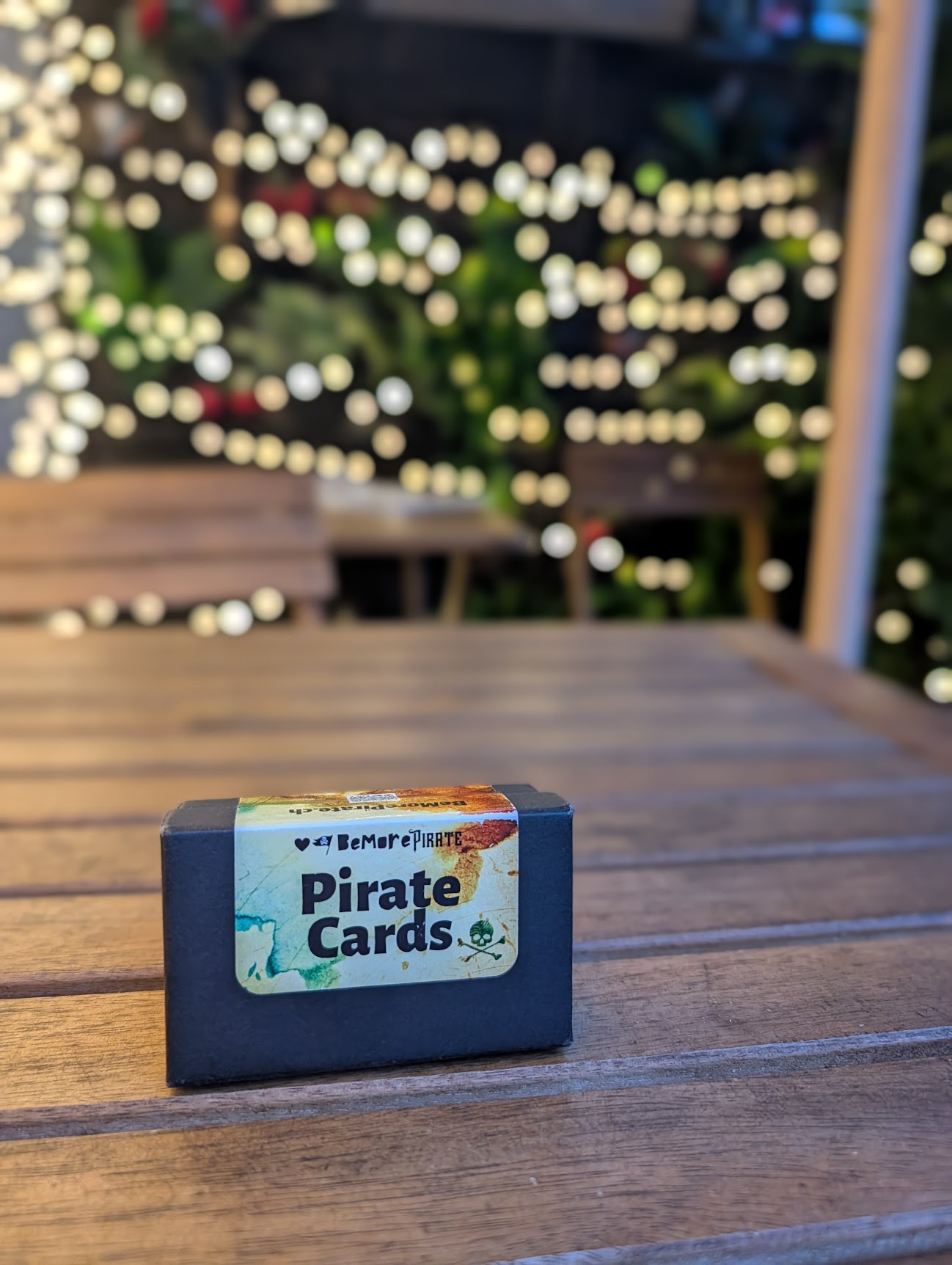 Pirate-Cards-Box auf einem Holztisch vor Lichterketten-Bokeh